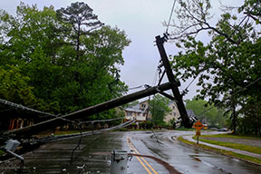 A wet road with a downed power poll laying across the road