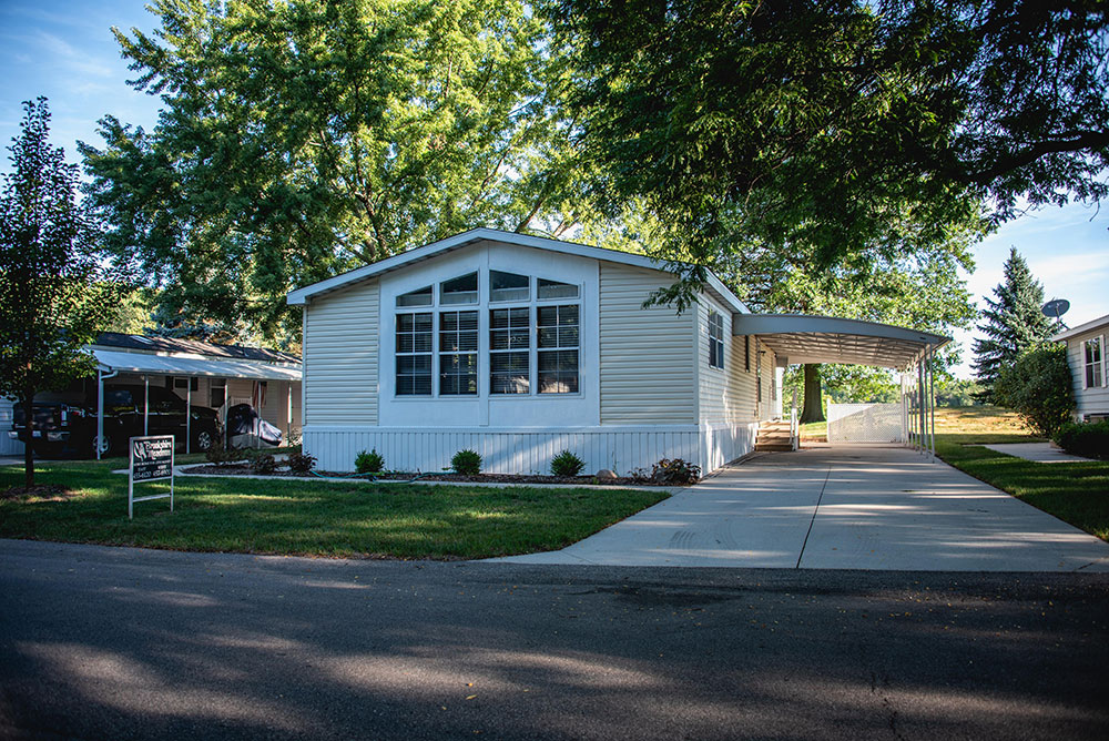 A manufactured home with a driveway and trees.