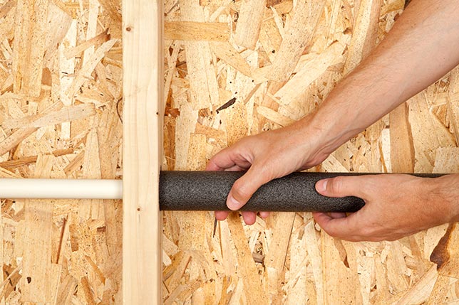 A close-up of hands wrapping a pipe with heat tape